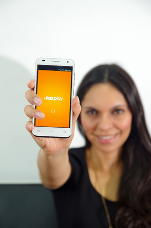 Quito, Ecuador - May 09, 2017: Beautiful woman with modern mobile phone in hands, login screen FOX play on Apple iPhone, a popular site to search and watch tv shows, pointing in from of her the cellphoneのeditorial素材
