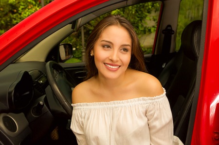 Beautiful sexy young woman inside of a red car smiling and wearing a white blouseの写真素材