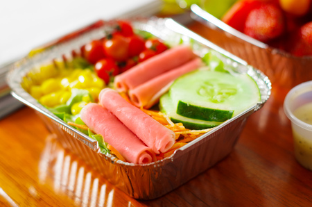 Delicious mediterranean-Style fresh salad with ham on aluminium box on wooden tableの写真素材