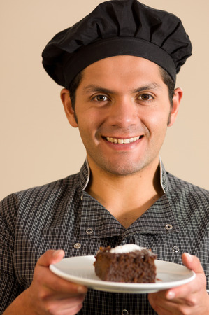 Handsome smiling man holding a piece of dark chocolate cake in a soft brown backgroundの写真素材