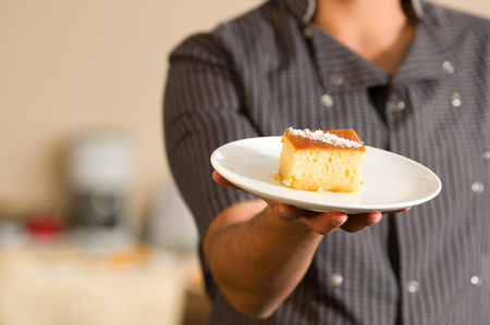 Man is holding in his hand a delicious turkish pastry with syrup revani over a white plateの写真素材