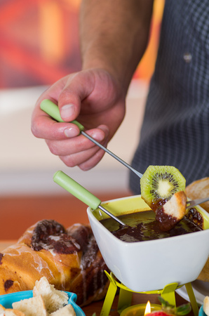 Delicious kiwi and apple in a metal stick covered with chocolate fondue inside of a white bowl on wooden tableの写真素材