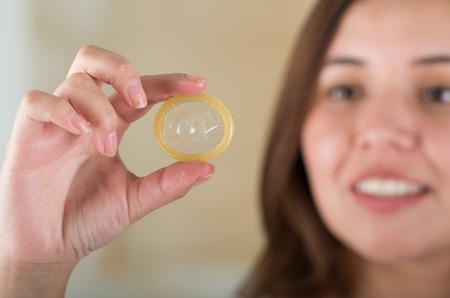 Close up of a beautiful young woman holding an open condom for aids prevention and birth controlの写真素材