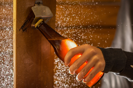 Close up of a man holding a bottle of craft beer using an opener, on wooden backgroundの写真素材