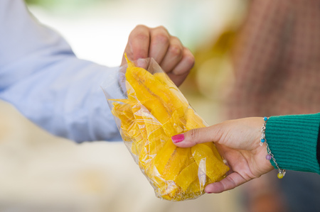 Young businessman eating a delicious slices fried plantain inside of a plastic bag in a public marketの写真素材