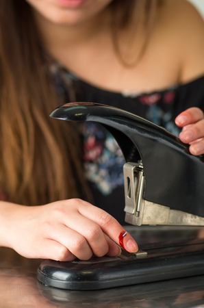 Beautiful young woman injured her finger using a stapler, bleedingの写真素材
