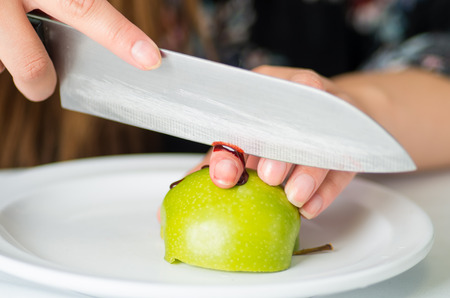 Close up of a young woman injured her fingers with a knife cutting an appleの写真素材
