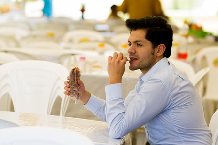 Handsome smiling young businessman eating a delicious slices fried sweet potato inside of a plastic bag in a public marketの写真素材