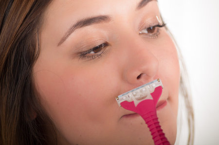 Close up of a beautiful young woman using a shaver pretending to shave her mustache, in a white backgroundの写真素材