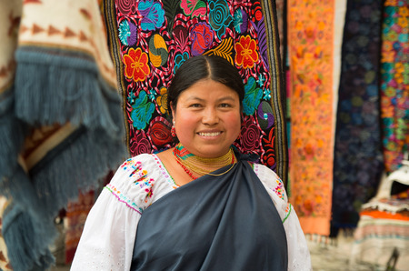 OTAVALO, ECUADOR - MAY 17, 2017: Close up of an unidentified hispanic indigenous woman wearing andean traditional clothing and necklace, posing for camera in colorful fabrics backgroundのeditorial素材