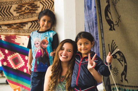 OTAVALO, ECUADOR - MAY 17, 2017: Beautiful young woman hugging to two beautiful little indigenous girls, in colorful fabrics backgroundのeditorial素材