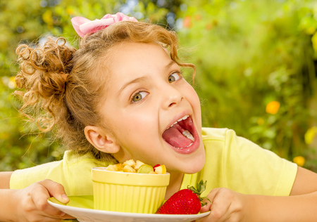 Close up of a beautiful young girl wearing a yellow t-shirt, preparing to eat a healthy fruit salad in a garden backgroundの写真素材