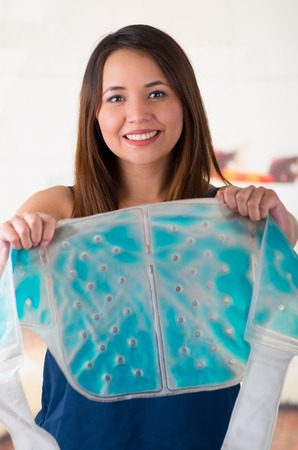 Close up of a beautiful smiling woman holding an ice gel pack with both hands, medical concept, in office backgroundの写真素材