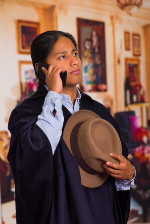 Close up portrait of young indigenous man wearing hat and poncho using cell phoneの写真素材