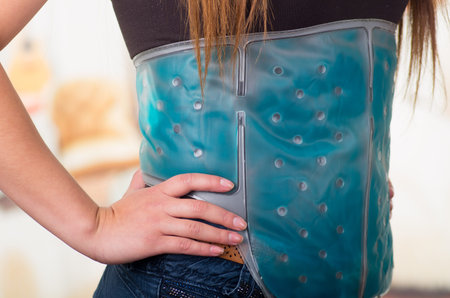 Close up of a female holding ice gel pack on her belly, medical concept, in office background