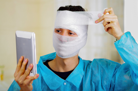 Portrait of a young man with trauma in his head and elastic bandaged around his head holding a tabletの写真素材