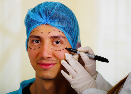 Surgeon drawing marks on male face. Plastic surgery conceptの写真素材