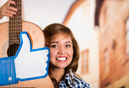 Quito, Ecuador - March 11, 2016: Close up of a smiling woman holding a guitar with a big like hand printed, in a blurred city backgroundのeditorial素材
