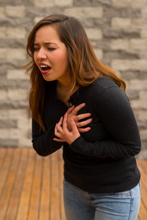 Young beautiful woman feeling bad and gripping her chest, cardiopulmonary resuscitation concept, in...