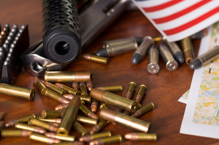 Close up of a shotgun and a revolver, cartridge belt with bullets with part of a blurred United States flag on a map, on wooden tableの写真素材
