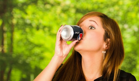 Quito, Ecuador - May 06, 2017: Pretty young woman drinking a pepsi in blurred green backgroundのeditorial素材