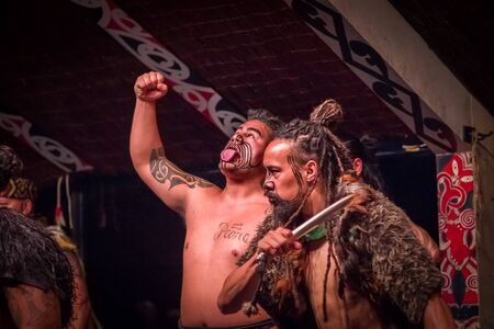 NORTH ISLAND, NEW ZEALAND- MAY 17, 2017: Tamaki Maori men one is sticking out tongue with traditionally tatooed face and in traditional dress at Maori Culture, Tamaki Cultural Village, Rotorua, New Zealandのeditorial素材
