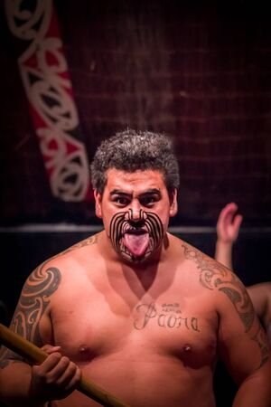 NORTH ISLAND, NEW ZEALAND- MAY 17, 2017: Tamaki Maori man sticking out tongue with traditionally tatooed face and in traditional dress at Maori Culture, Tamaki Cultural Village, Rotorua, New Zealandのeditorial素材