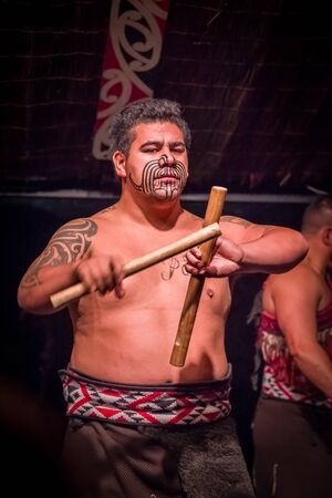NORTH ISLAND, NEW ZEALAND- MAY 17, 2017: Close up of a Tamaki Maori man with traditionally tatooed face and in traditional dress at Maori Culture village holding a wooden sticks in Tamaki Cultural Village, Rotorua, New Zealandのeditorial素材