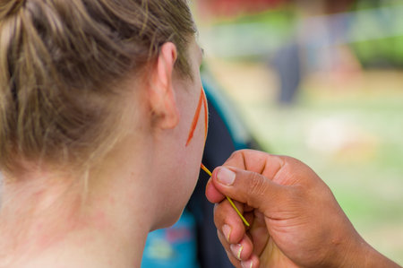 Young tourist painting her face using achiote seeds from these spiny red pods with natural color,...