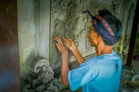 BALI, INDONESIA - MARCH 08, 2017: Man using a chisel to do art on a wall of cement, in Denpasar Bali located in Indonesiaのeditorial素材