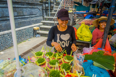 BALI, INDONESIA - MARCH 08, 2017: Unidentified woman do an arrangement of flowers inside of a box made of leafs in a market, on a table, in the city of Denpasar in Indonesiaのeditorial素材