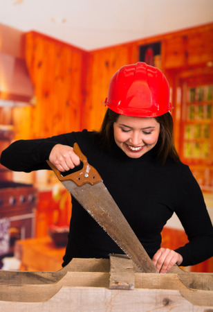 Beautiful young woman cutting wood with a sawの写真素材