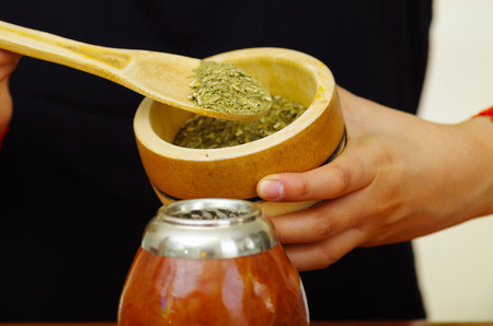 Woman holding bowl with green herbs preparing traditional cup of popular drink called mate, typical metal straw sticking upの写真素材