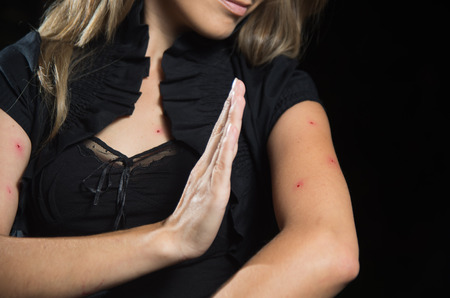 Young woman is using her hand to kill a mosquito over her arm, in a black backgroundの写真素材