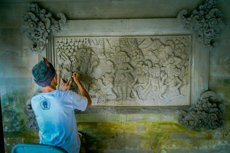 BALI, INDONESIA - MARCH 08, 2017: Man using a chisel to do art on a wall of cement, in Denpasar Bali located in Indonesiaのeditorial素材
