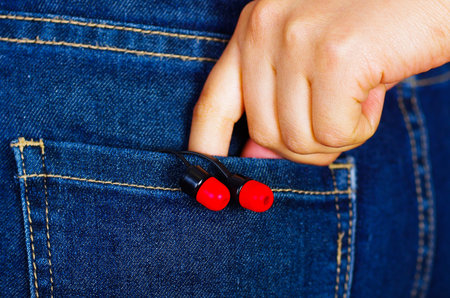 Woman hand holding a black with red headphones inside of jeans back pocket