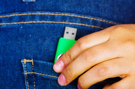 Woman hand putting a green flash memory inside of jeans back pocket