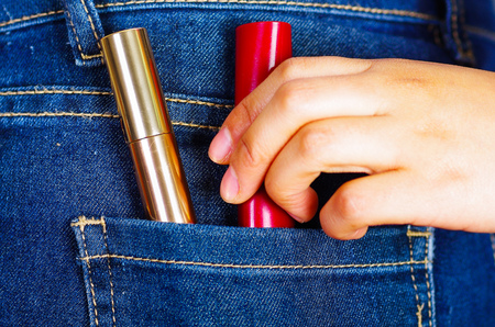 Woman hand holding a red and golden lipsticks inside of jeans back pocketの写真素材