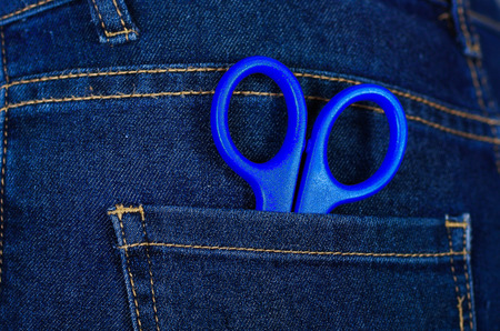 Blue scissors inside of jeans back pocket with a handの写真素材