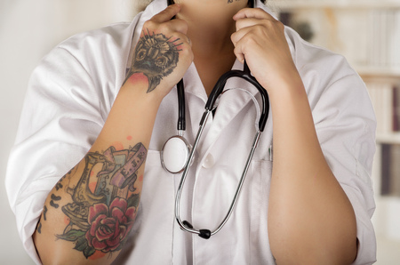 Close up of a tattooed young doctor with a stethoscope around her neck, in office backgroundの写真素材