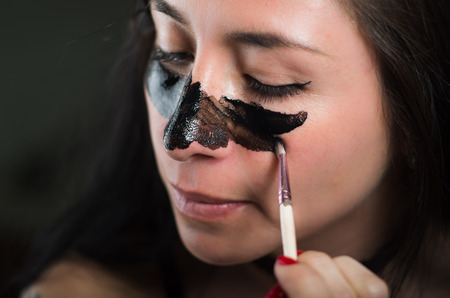 Close up of a beauty young woman aplying in her face a black mask to clean the skinの写真素材