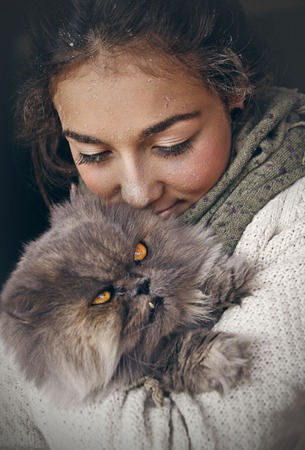 Young beautiful woman hugging her persian cat, wearing a scarf around her neck in a black backgroundの写真素材