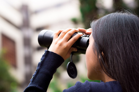 Young woman stalking with a black binoculars in a city backgroundの写真素材