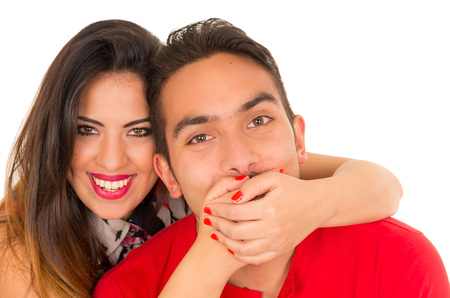Close up of happy couple isolated on white background. Attractive man and woman being playful, woman putting her hands over his boyfriend mouthの写真素材