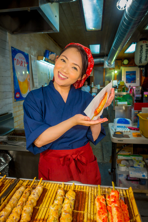 KYOTO, JAPAN - JULY 05, 2017: Unidentified smiling woman holding in her hand a brochette, sold at Nishiki Market in Kyotoのeditorial素材