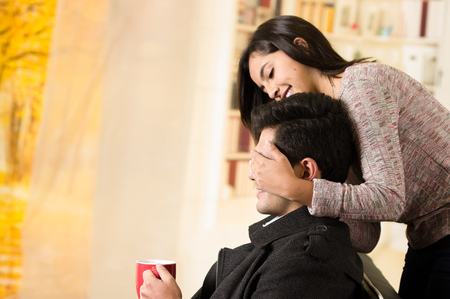 Beautiful young couple in love, girlfriend is covering the eyes of his boyfriend in a office backgroundの写真素材