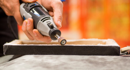 Closeup of a hardworker man using a polisher in a wooden frame, on a gray table in a blurred...