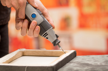 Closeup of a hardworker man drilling a wooden frame with his drill over a gray table in a blurred backgroundの写真素材