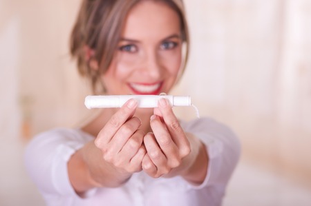 Close up of a young woman pointing in front of her a menstruation cotton tampon and manipulating the tampon, in a blurred backgroundの写真素材