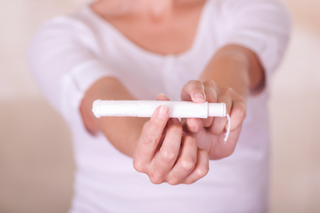 Close up of a young woman pointing in front of her a menstruation cotton tampon and manipulating the tampon, in a blurred backgroundの写真素材